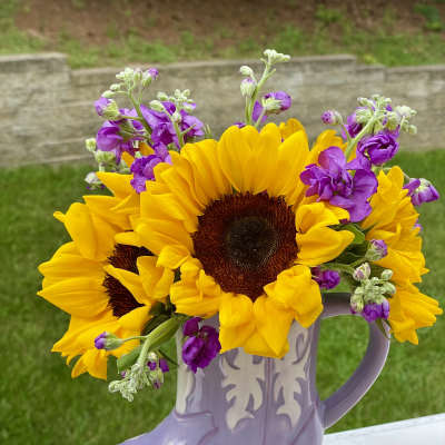 Sunflowers and purple flowers arranged in a lavender boot-shaped vase