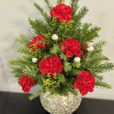 Red carnations in a glittery round vase with evergreen sprigs
