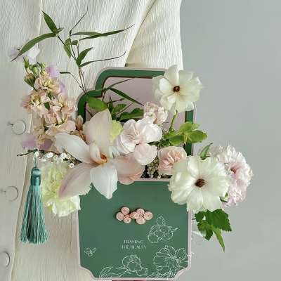 Pastel floral arrangement in a green decorative box with a tassel
