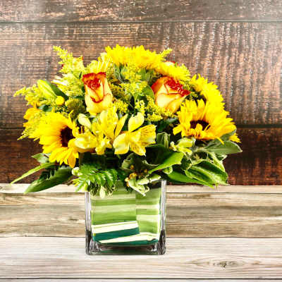Yellow sunflowers and roses arranged in a square glass vase