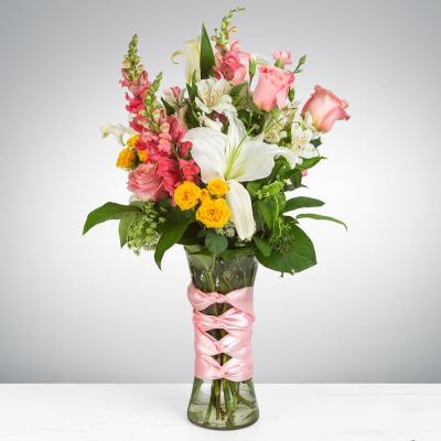 Pink roses and white lilies in a tall glass vase with a pink ribbon
