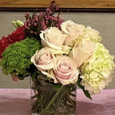 Bouquet of pale roses, hydrangea, and green filler in a glass vase