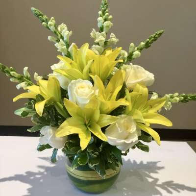 Yellow lilies and white roses arranged in a green glass vase