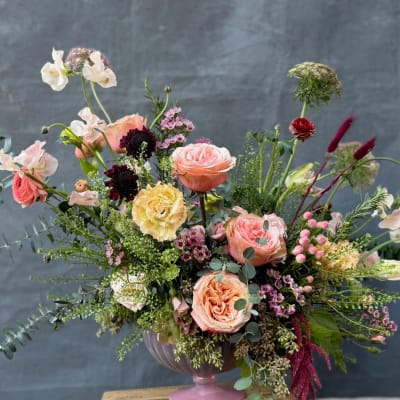 Mixed bouquet of peach, pink, and cream flowers in a pink vase