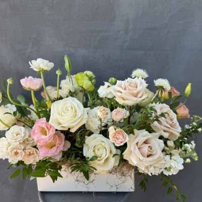Pastel roses and mixed blooms arranged in a white rectangular vase