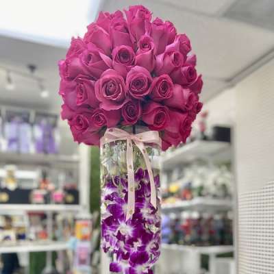 Tall glass vase with hot pink roses on top and submerged purple orchids tied with a ribbon.