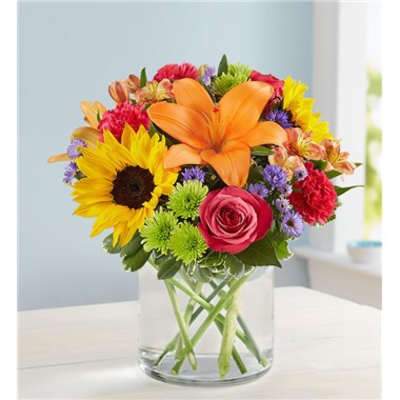 Colorful mixed bouquet in a clear glass vase with sunflower, lily, and rose blooms