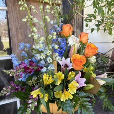 Mixed bouquet with orange roses, lilies, and blue flowers in a basket