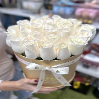 Round gold hatbox filled with tightly packed white roses, tied with a white ribbon.