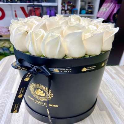 Round black hat box filled with tightly packed ivory roses and tied with a black ribbon