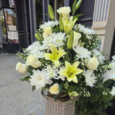 Tall white and pale yellow floral arrangement in a decorative pedestal vase