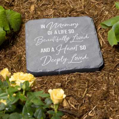Memorial stone with engraved text in a garden bed beside yellow roses