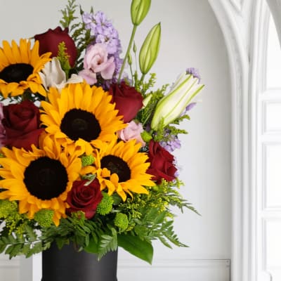 Bouquet of sunflowers, red roses, lilies, and lavender flowers in a black box