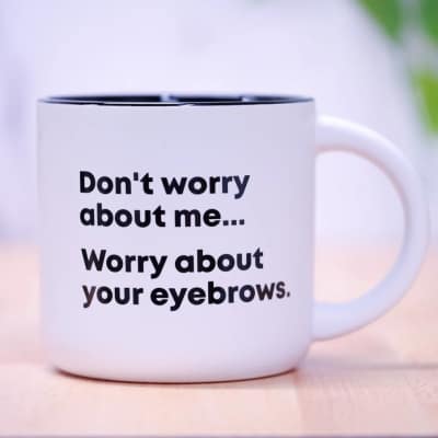 White mug with black text reading "Don't worry about me... Worry about your eyebrows."