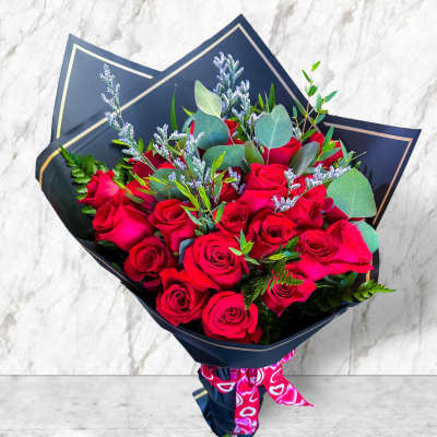 Bouquet of red roses wrapped in dark paper with a pink ribbon