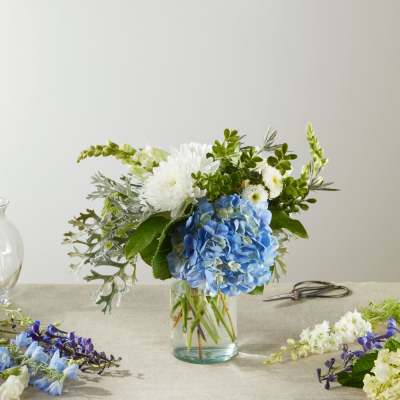 Blue hydrangea and white flowers in a clear glass vase