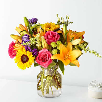 Mixed bouquet of lilies, roses, and a sunflower in a glass vase