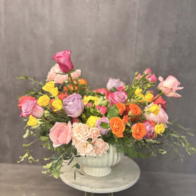 Mixed bouquet of pink, yellow, orange, and lavender roses in a white vase