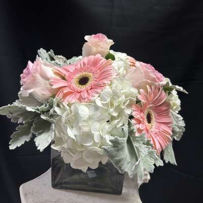 Pink gerbera daisies and pale roses in a square glass vase