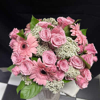 Pink roses and gerbera daisies arranged in a bouquet with white filler flowers.