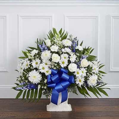 White and blue floral standing spray with a large ribbon on a pedestal.