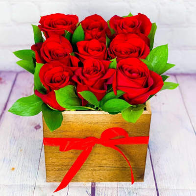 Red roses arranged in a wooden box with a red ribbon