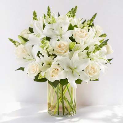 White lilies and cream roses arranged in a clear glass vase.