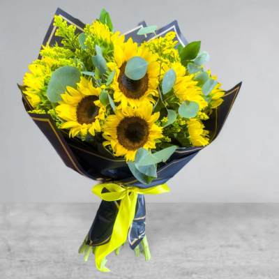 Bouquet of yellow sunflowers wrapped in dark paper with a bright ribbon