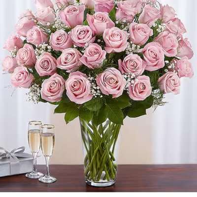 Pink roses arranged in a clear glass vase with a gift box and champagne flutes nearby