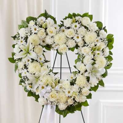 Heart-shaped white floral wreath on a black stand