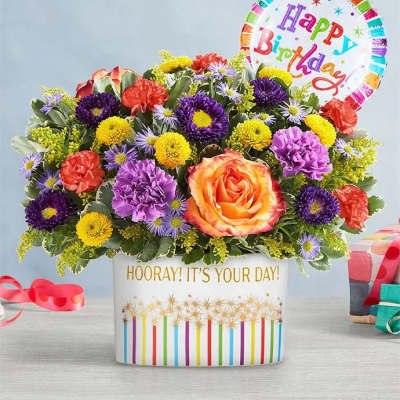 Colorful mixed flower arrangement in a birthday container with a balloon