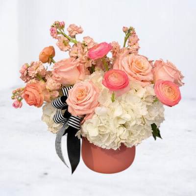 Pink and peach flowers arranged in a coral vase with a striped ribbon
