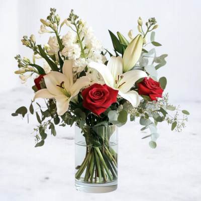 Arrangement of white lilies, white stock, and red roses in a clear glass vase