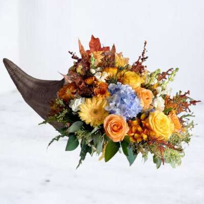Autumn bouquet with yellow, orange, blue, and white flowers in a horn-shaped container