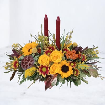 Low floral centerpiece with yellow blooms and two red taper candles
