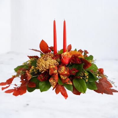 Low autumn floral centerpiece with red candles and orange blooms