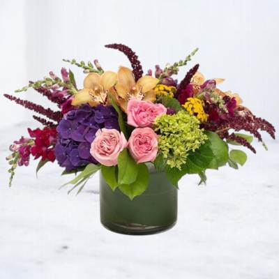 Mixed bouquet in a dark green glass vase with pink, purple, yellow, and peach flowers.
