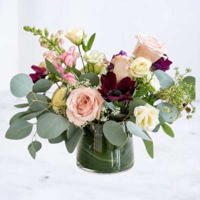 Mixed bouquet of roses, snapdragons, and dark blooms in a glass vase
