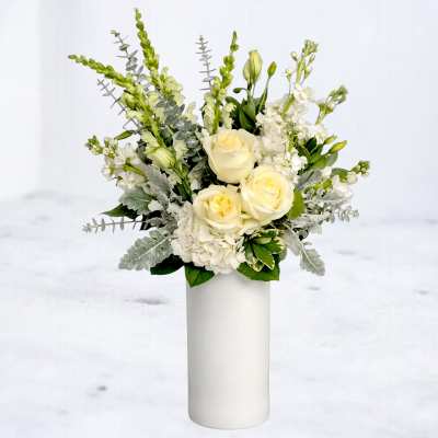 White roses and white flowers arranged in a tall white vase