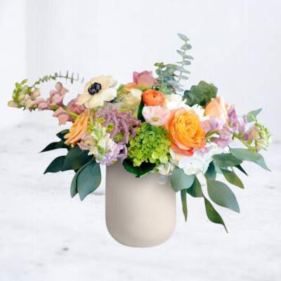 Mixed pastel flower arrangement in a beige vase