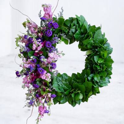 Green foliage wreath with cascading pink and purple flowers on one side