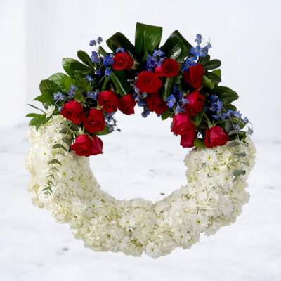 Circular floral wreath with white flowers, red roses, and blue accents