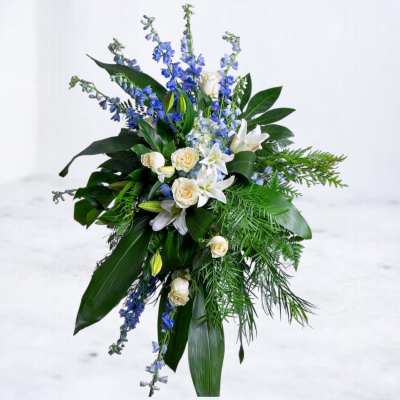 Tall bouquet of white roses, lilies, and blue flowers with dark foliage