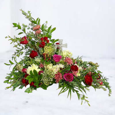 Low floral arrangement with red and pink roses and a clear glass cross