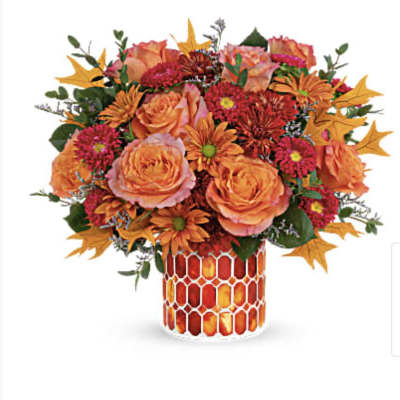 Orange roses and mums in a patterned vase with autumn leaf accents