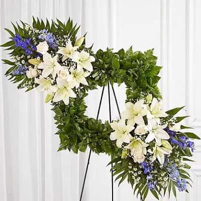 Two floral wreaths on black stands with white lilies and blue flowers