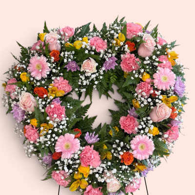 Heart-shaped floral wreath with pink, yellow, and white blooms on a stand