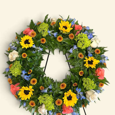Circular floral wreath with sunflowers, roses, and blue flowers on a stand