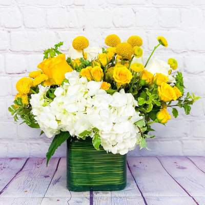 Yellow roses and white hydrangeas in a green square vase