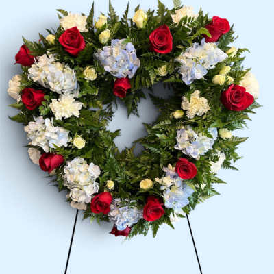 Heart-shaped floral wreath with red roses and pale hydrangeas on a stand